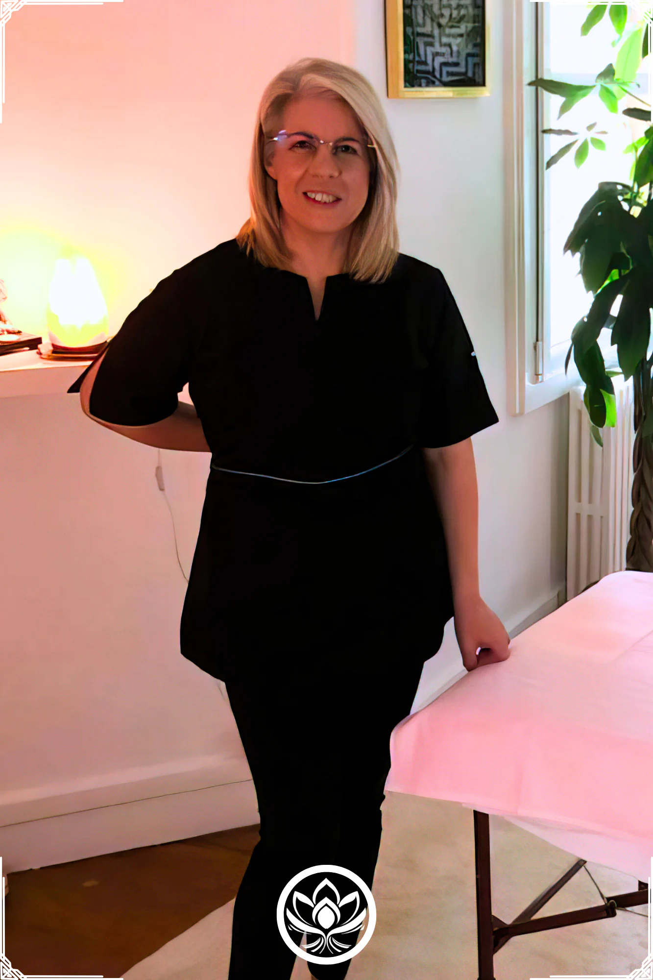 Maria Nikita praticienne souriante en tenue noire dans le cabinet, prete pour un massage therapeutique, kobido, ayurvedique ou bowen.